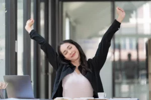 female-entrepreneur-sitting-at-desk-with-laptop-in-front-of-her-stretching